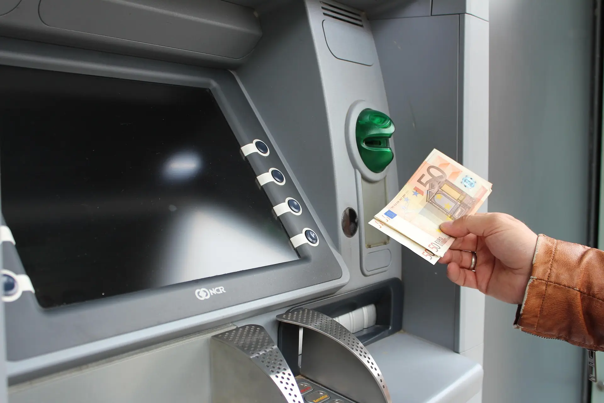 Kamay na may hawak na banknotes sa tabi ng cash slot ng ATM