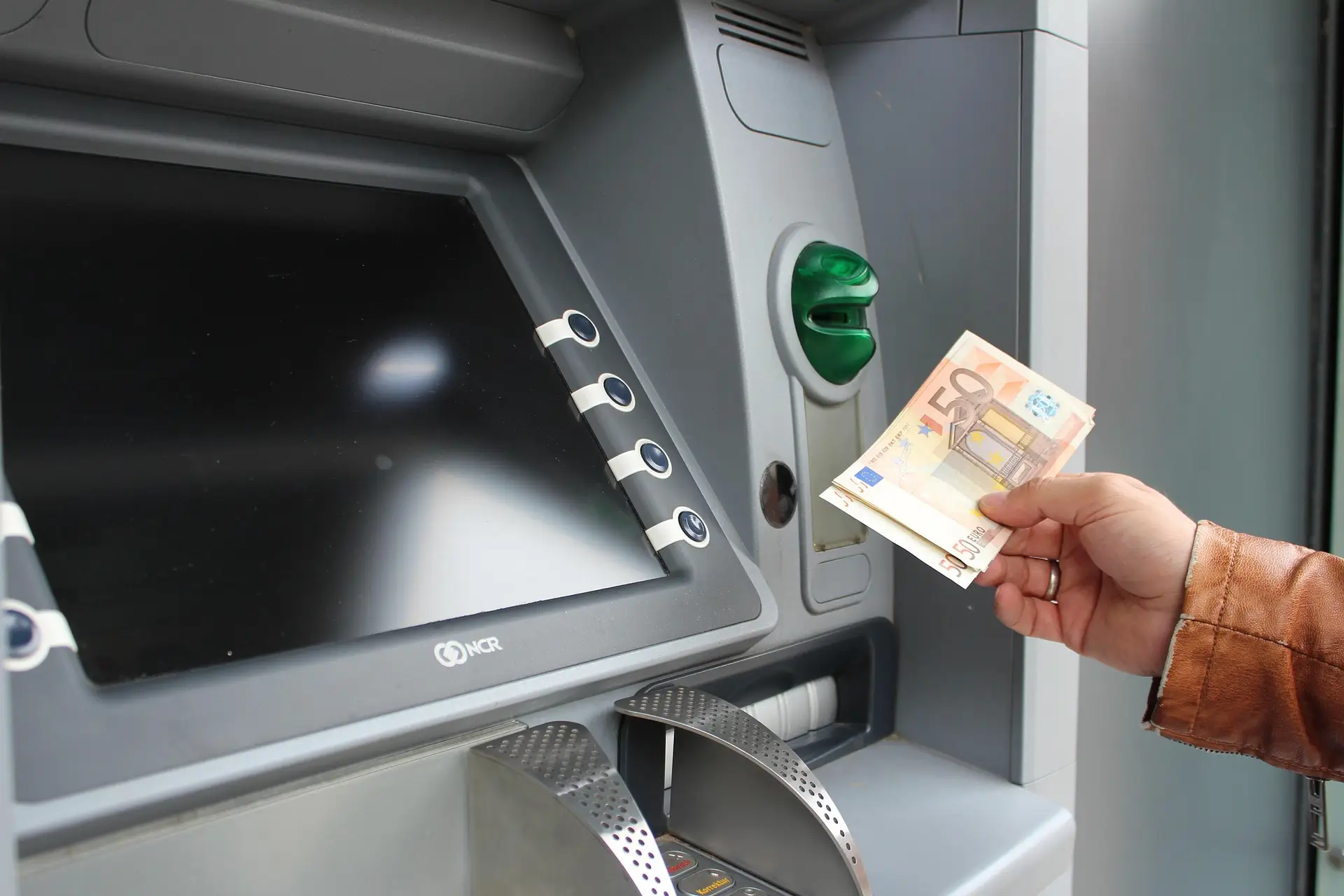 Kamay na may hawak na perang papel sa harap ng keypad ng cash machine